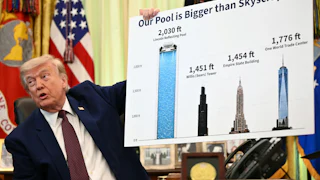 Donald Trump speaks while sitting at his desk in the Oval Office. He holds up a poster comparing the length of the Reflecting Pool to heights of various skyscrapers.