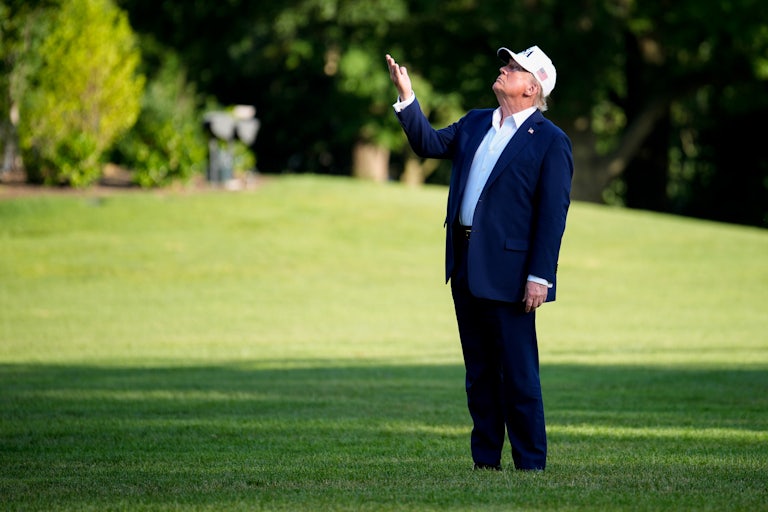Donald Trump raises his hand and looks up while standing on the White House lawn