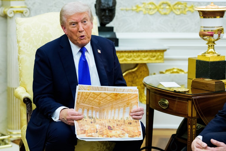 Donald Trump sits in the Oval Office and speaks while holding up a rendering of the gilded ballroom he's building at the White House