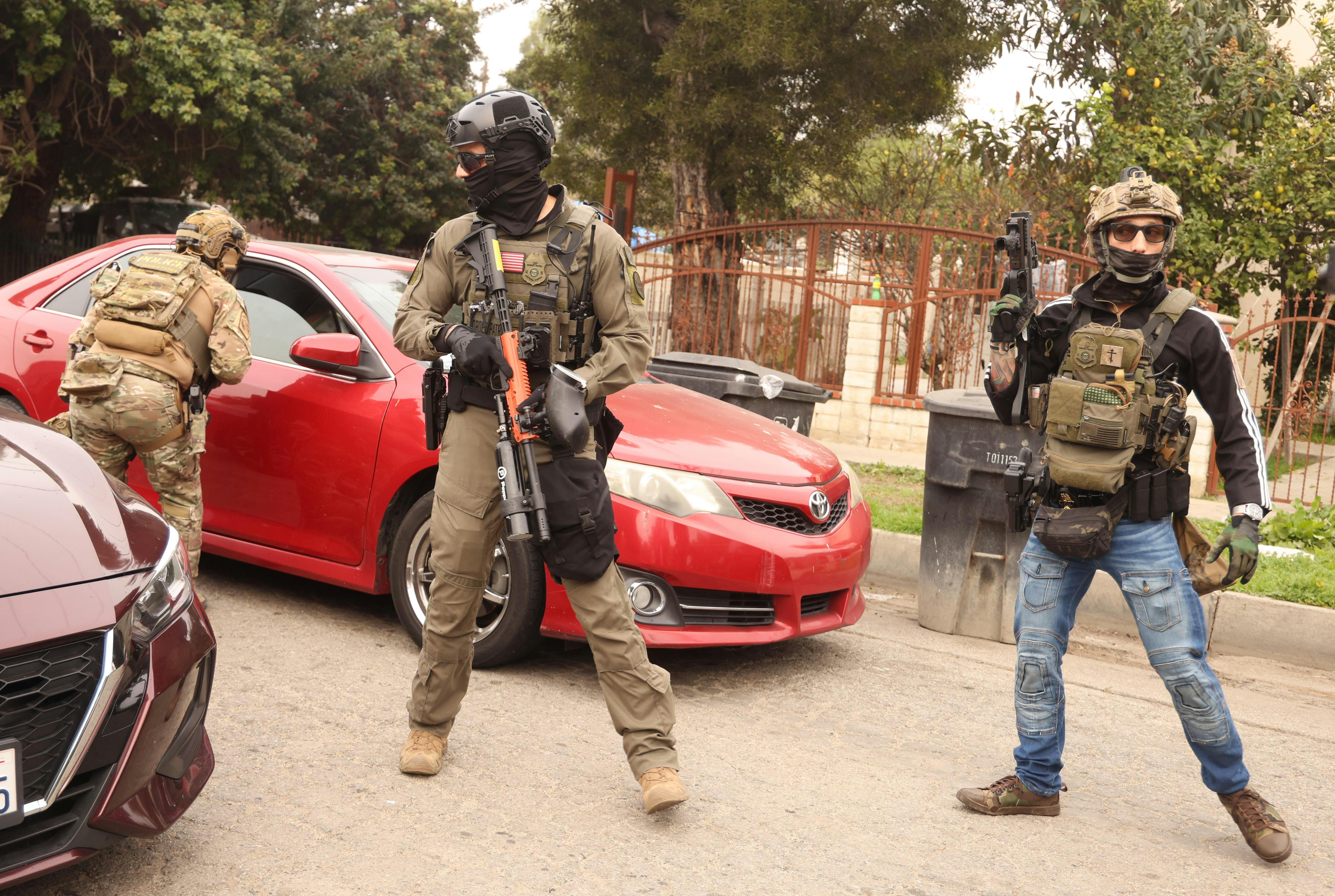 Masked federal immigration agents stand next to cars