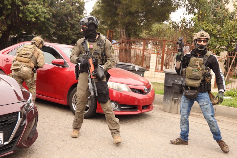 Masked federal immigration agents stand next to cars