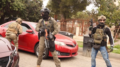 Masked federal immigration agents stand next to cars