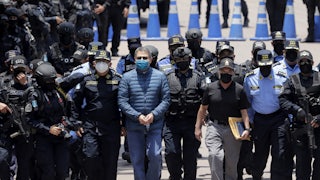 Former President of Honduras Juan Orlando Hernandez, handcuffed and masked, walks with members of the police.
