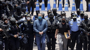 Former President of Honduras Juan Orlando Hernandez, handcuffed and masked, walks with members of the police.