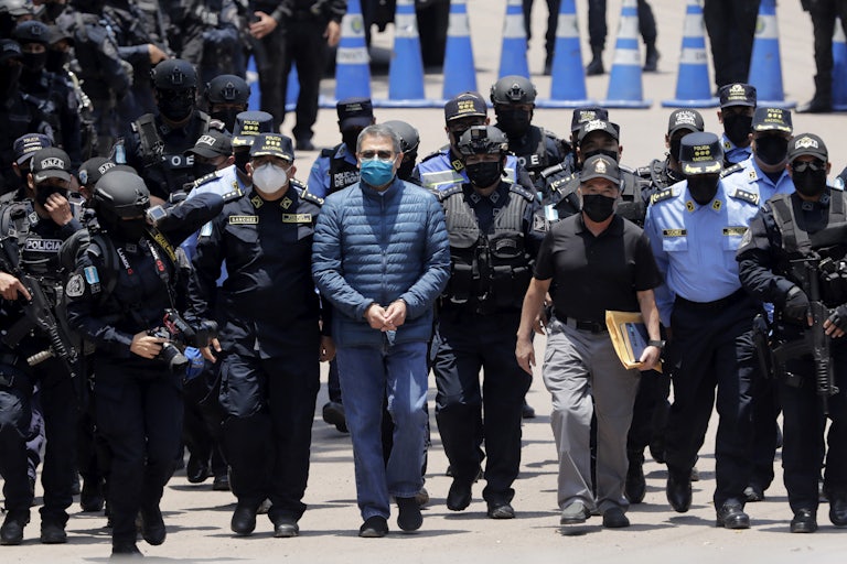 Former President of Honduras Juan Orlando Hernandez, handcuffed and masked, walks with members of the police.