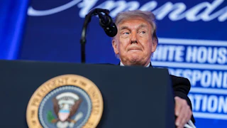Donald Trump presses his lips together while standing at a podium during the White House Correspondents Dinner.