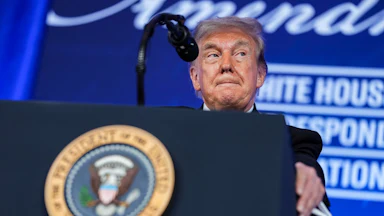 Donald Trump presses his lips together while standing at a podium during the White House Correspondents Dinner.
