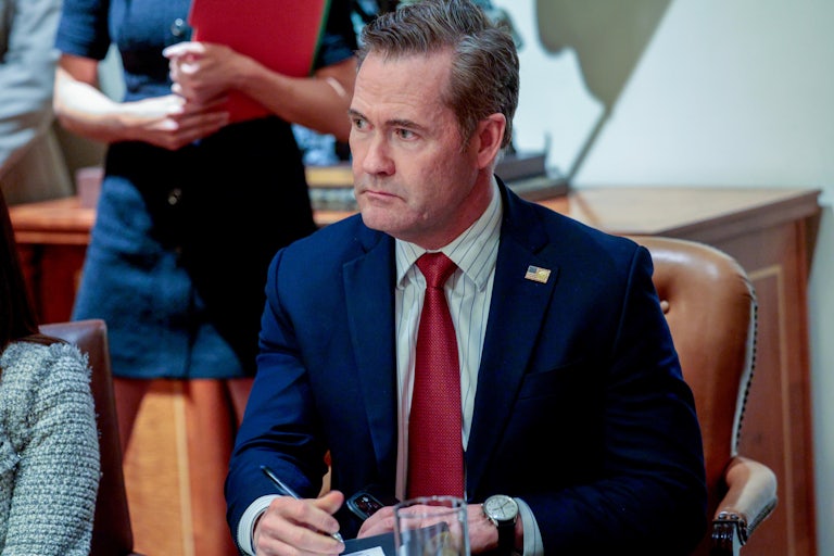 Mike Waltz sits in a Trump Cabinet meeting looking grim. He holds a pen in one hand and his phone in the other.