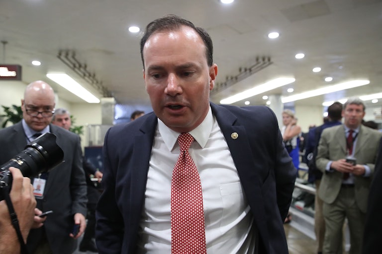Mike Lee walks while being confronted by reporters.