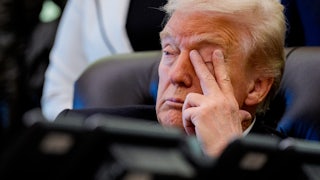 Donald Trump touches his eye with two fingers while sitting at his desk in the Oval Office