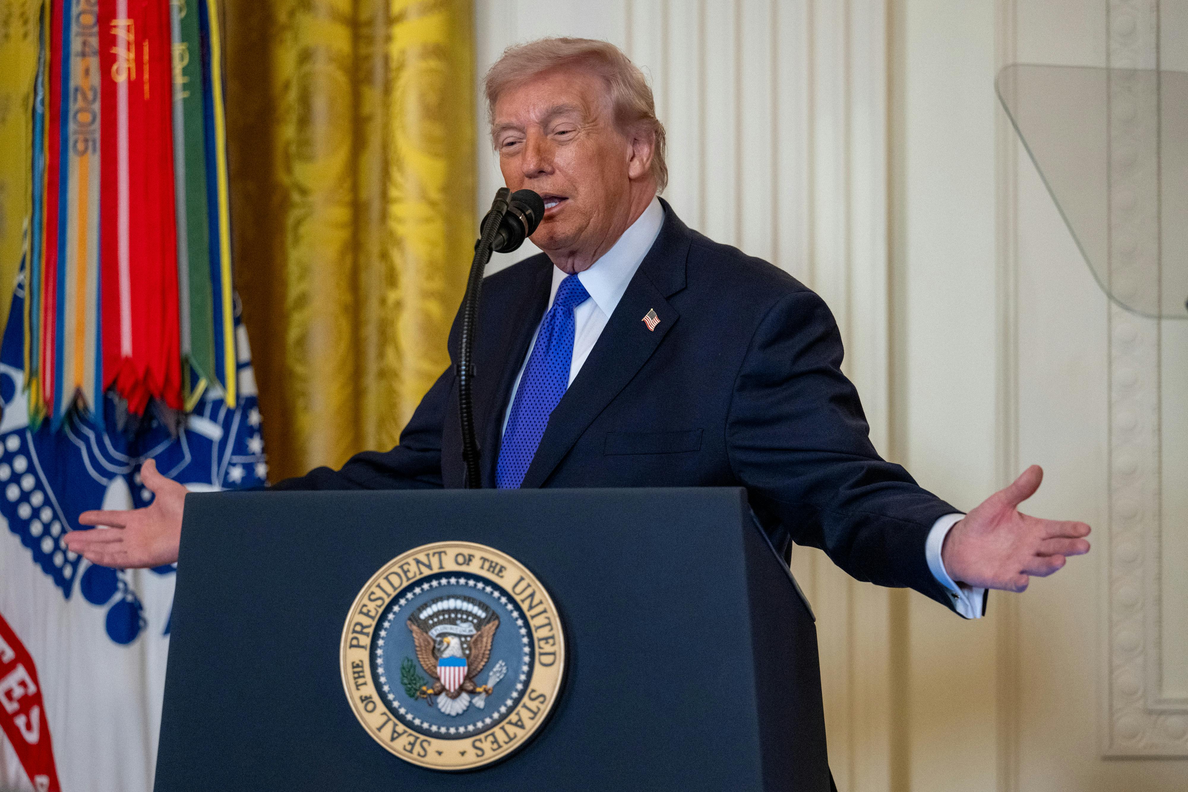 Donald Trump holds his arms out to the side while speaking at a podium