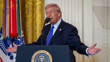 Donald Trump holds his arms out to the side while speaking at a podium