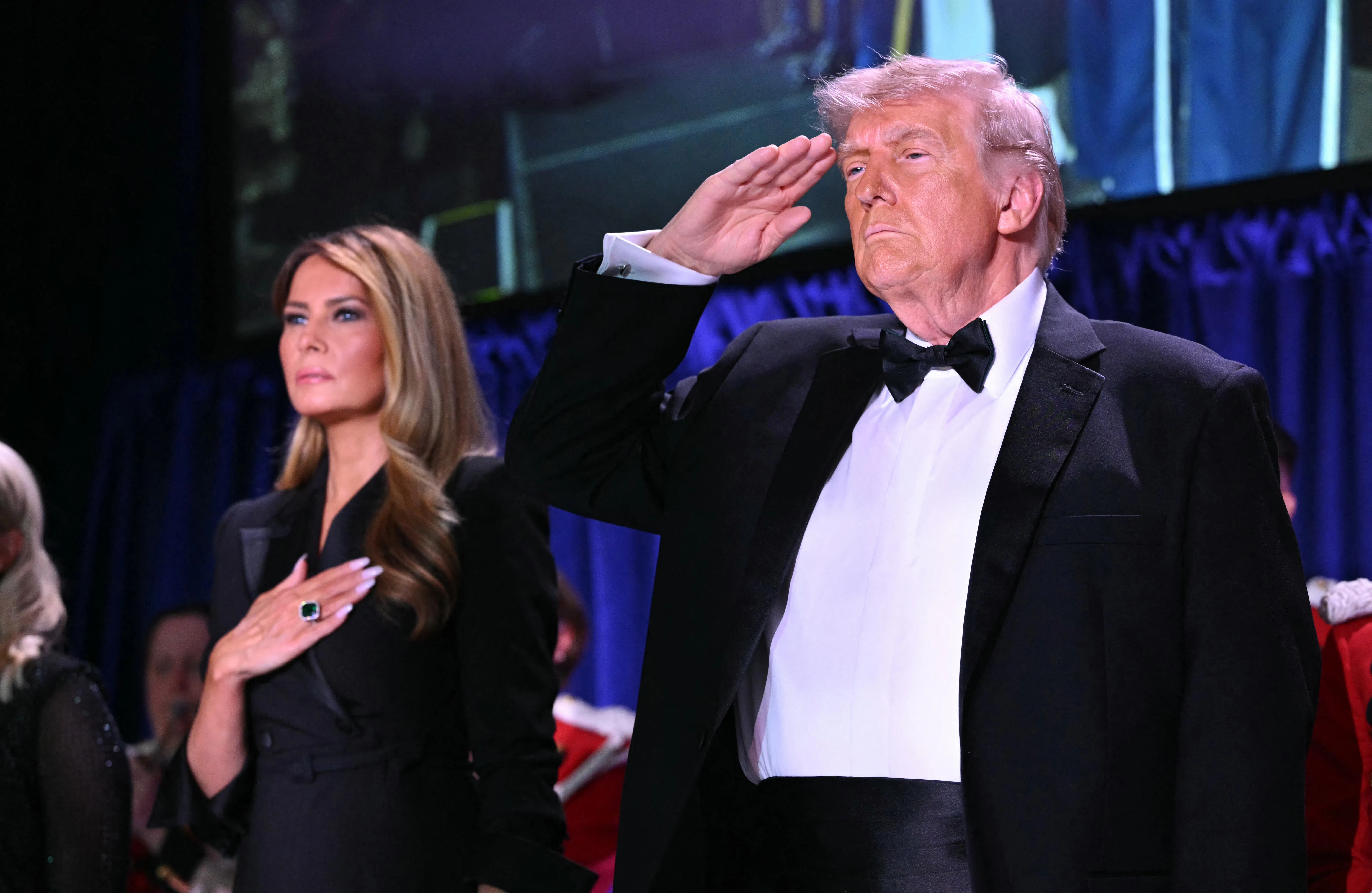 President Donald Trump salutes and First Lady Melania Trump puts a hand on her heart.
