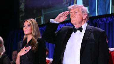 President Donald Trump salutes and First Lady Melania Trump puts a hand on her heart.