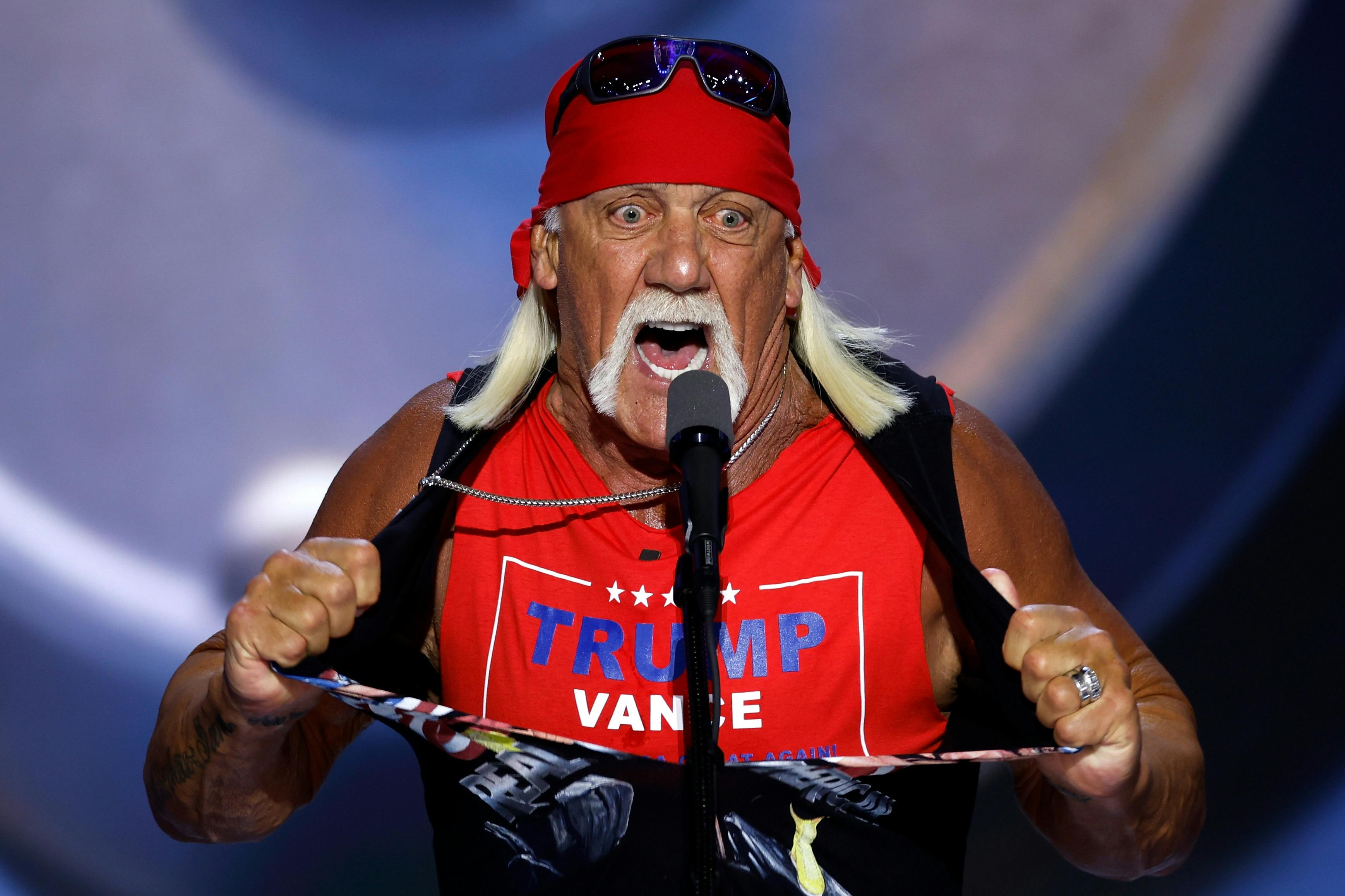 Hulk Hogan stands in front of a microphone and rips his shirt to reveal a "Trump Vance" T-shirt beneath.