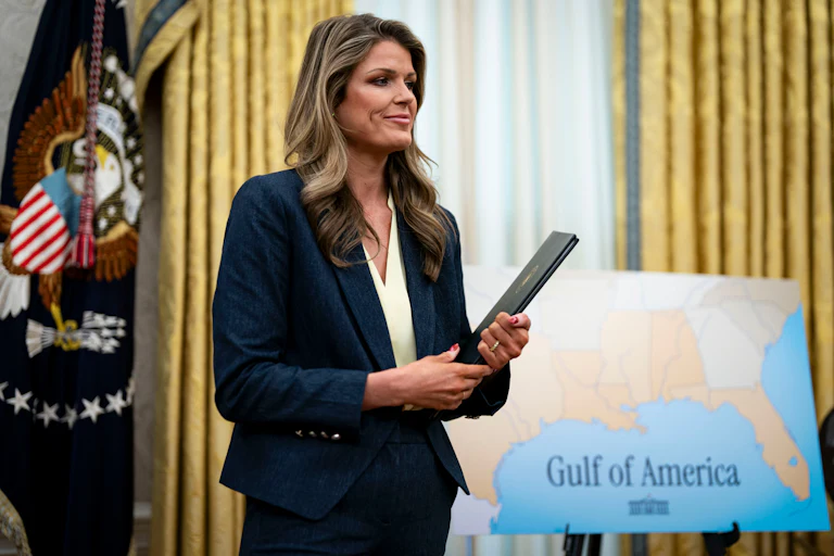 Lindsey Halligan holds a folder while standing next to a large map that says "Gulf of America"