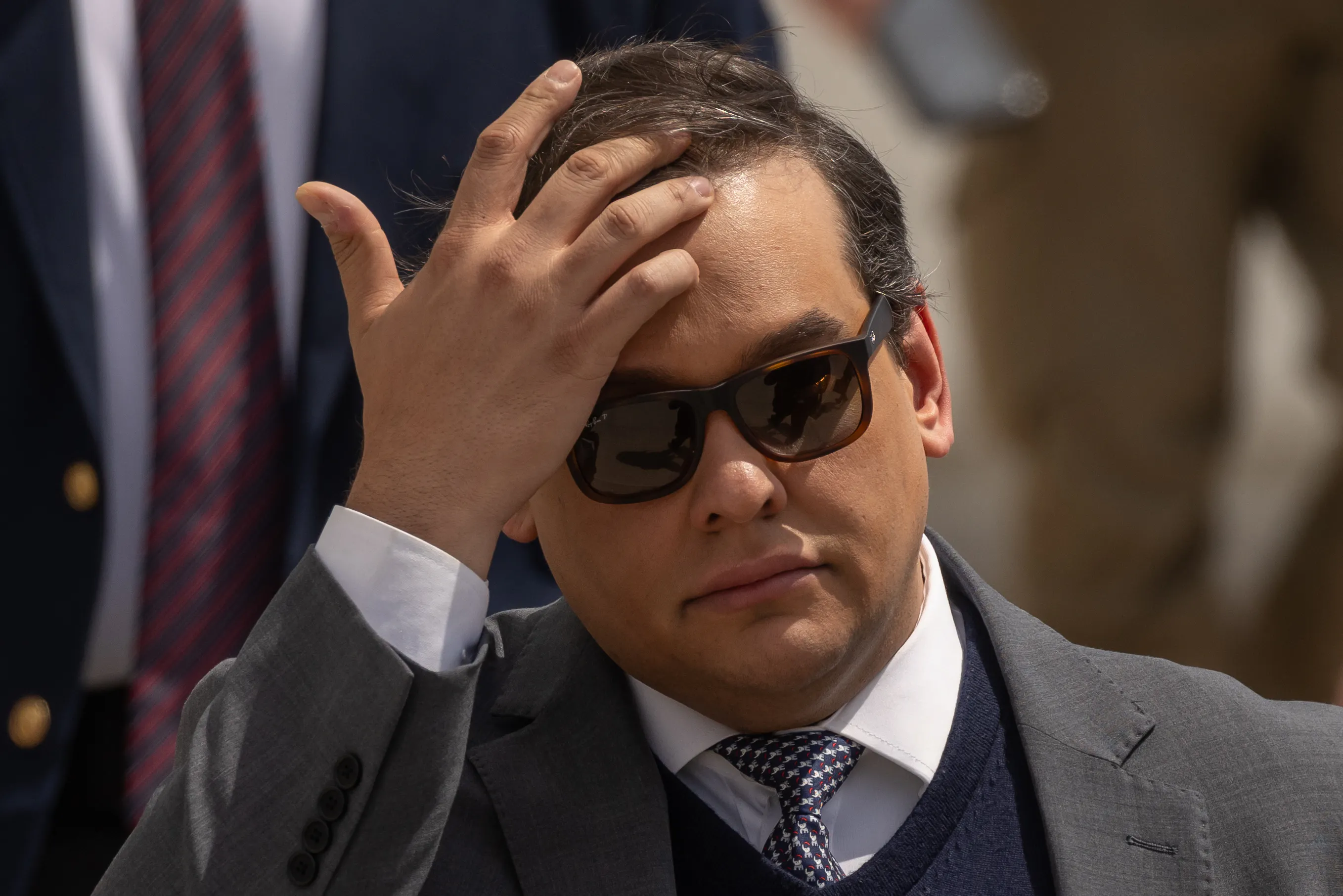 Former Representative George Santos touches his forehead while walking