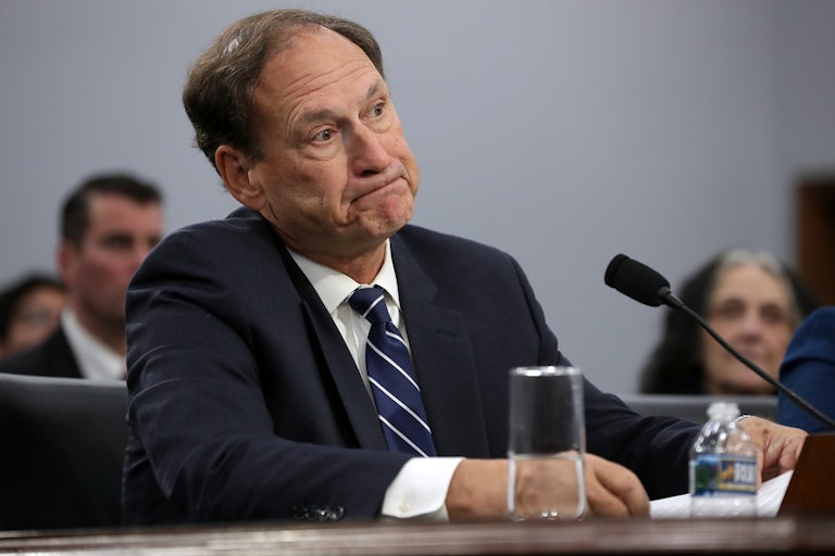 Samuel Alito frowns as he sits in front of a microphone