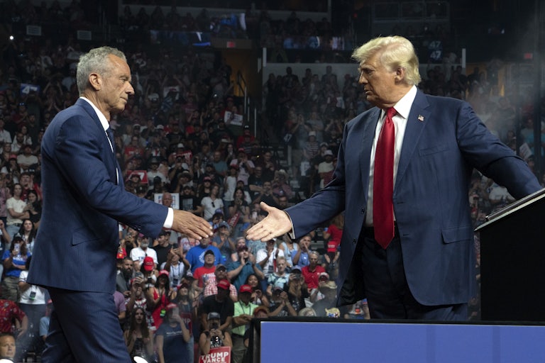 Robert F. Kennedy Jr. walks toward Trump to shake his hand. Both are on stage at a campaign rally.