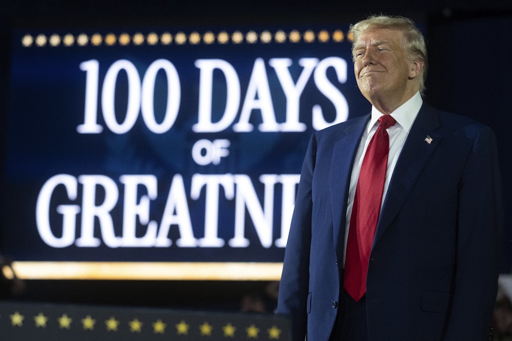 Donald Trump delivers a speech marking his 100th day in office in front of an illuminated screen that reads "100 days of greatness."