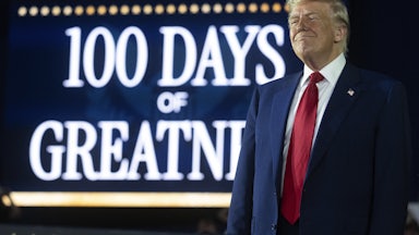 Donald Trump delivers a speech marking his 100th day in office in front of an illuminated screen that reads "100 days of greatness."