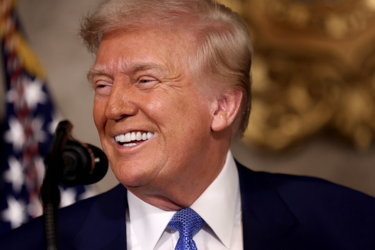 Donald Trump smiles while a standing mic is in front of his mouth.