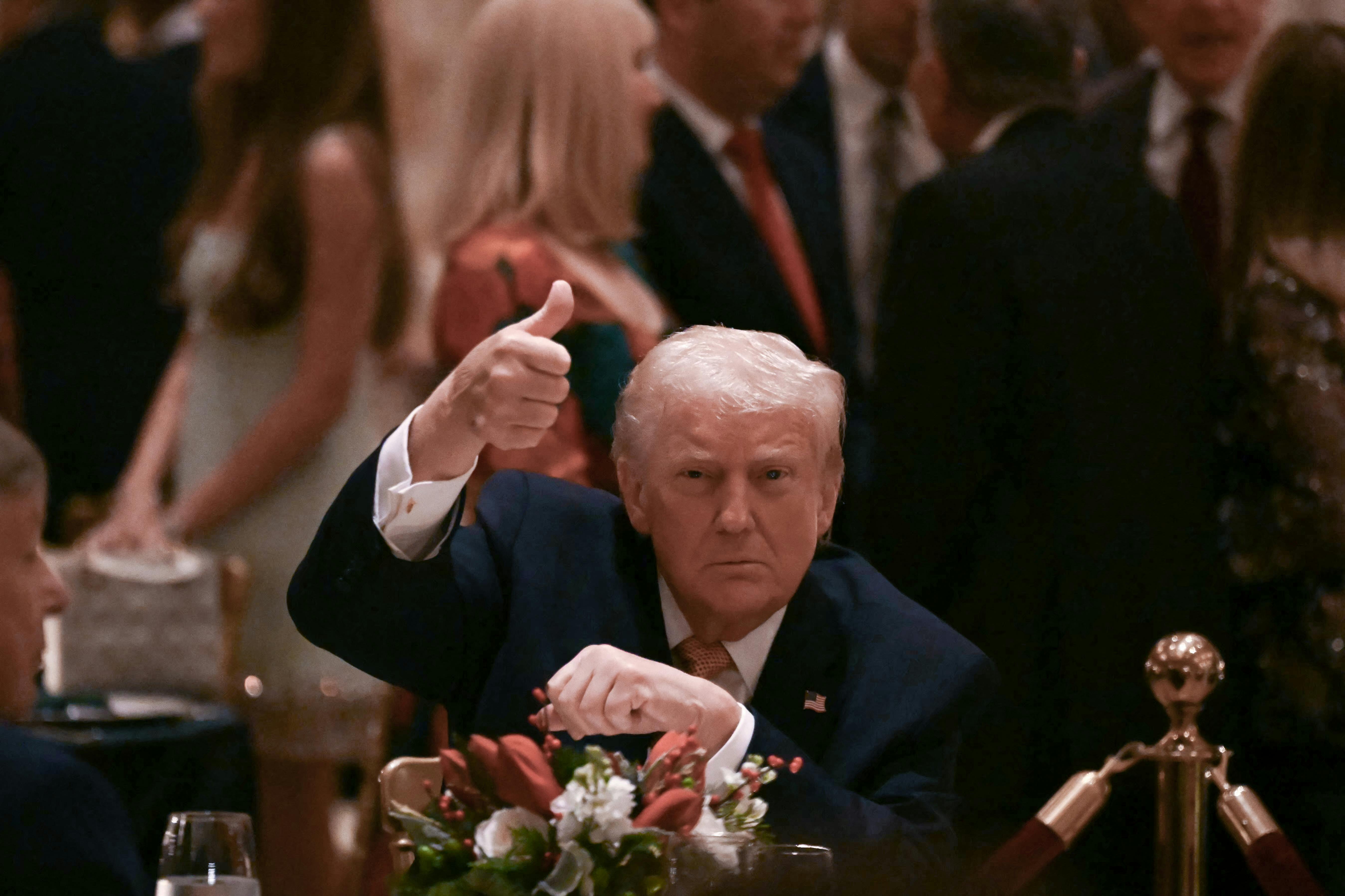 Donald Trump holds a thumbs up for the camera while seated at a table at Mar-a-Lago.