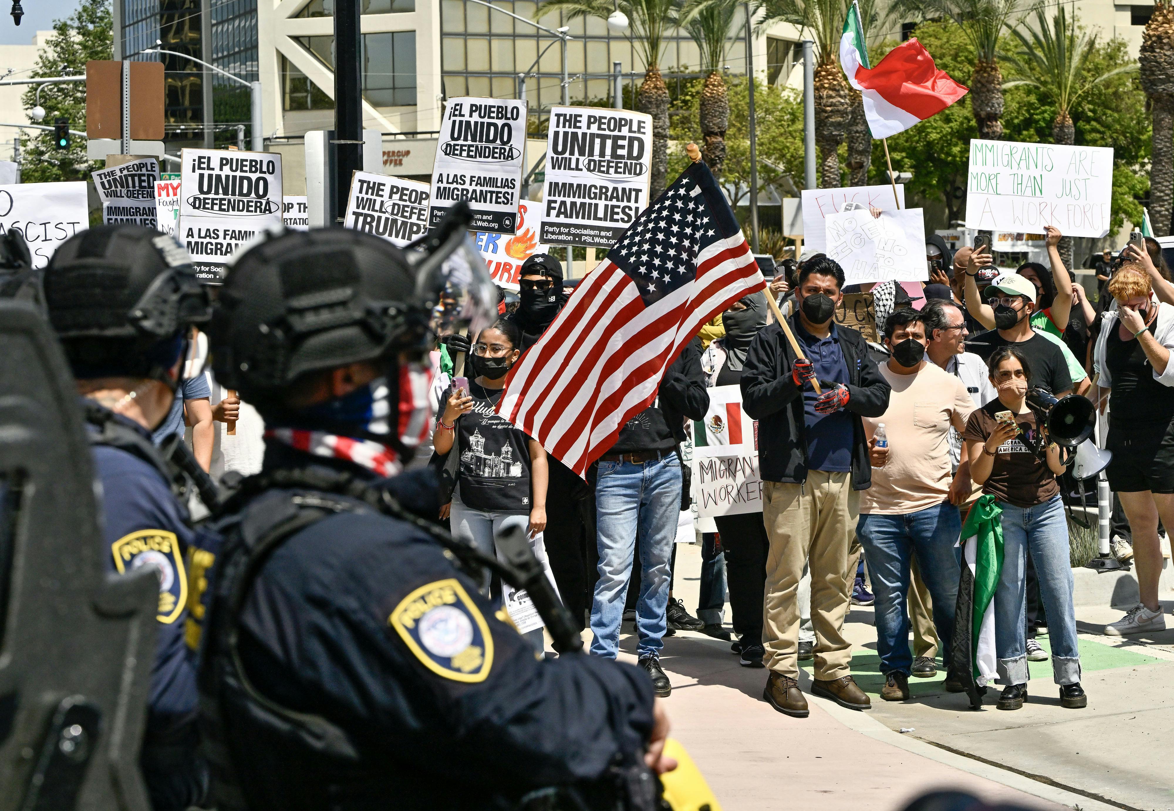 Anti-ICE protesters hold signs and U.S. flags as police watch.