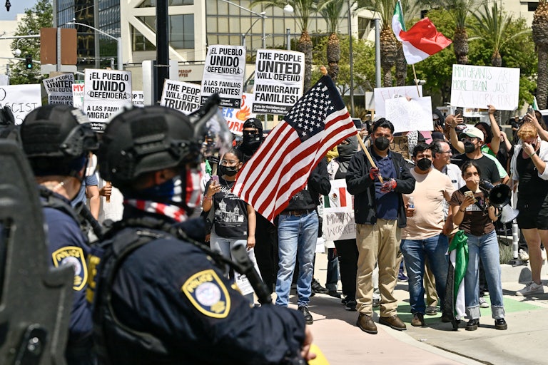 Anti-ICE protesters hold signs and U.S. flags as police watch.