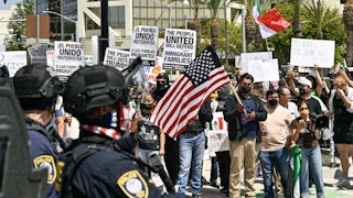 Anti-ICE protesters hold signs and U.S. flags as police watch.