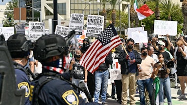 Anti-ICE protesters hold signs and U.S. flags as police watch.