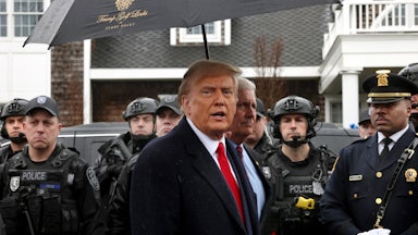Donald Trump stands under an umbrella, surrounded by police officers