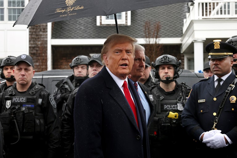Donald Trump stands under an umbrella, surrounded by police officers