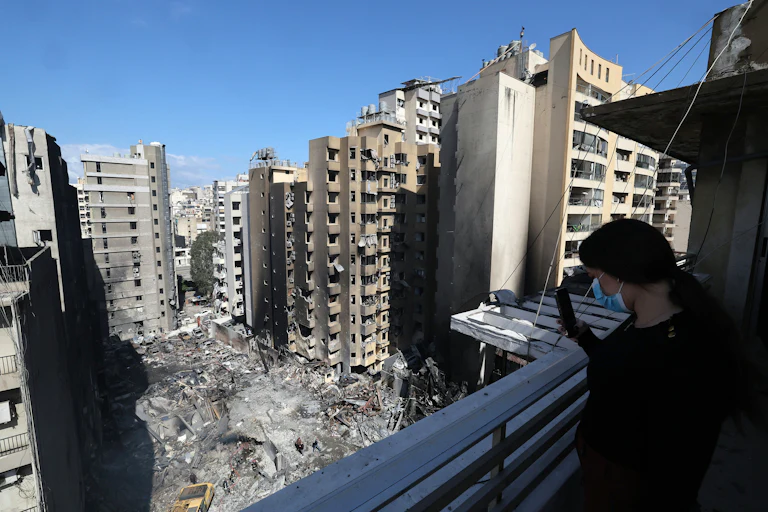 A woman wearing a face mask on a balcony takes a picture with her phone of Lebanese first responders searching under the rubble