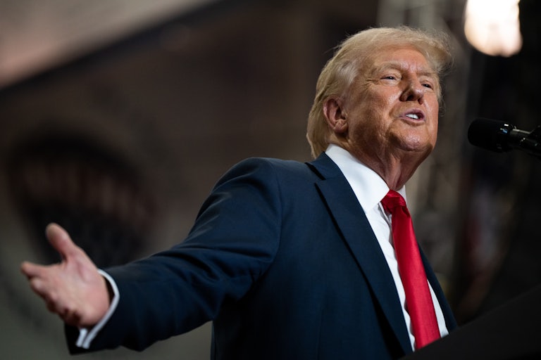 Donald Trump speaks into a mic and splays his arms out