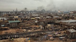 Smoke billows from logs covered with soil next to sheds in Lagos.