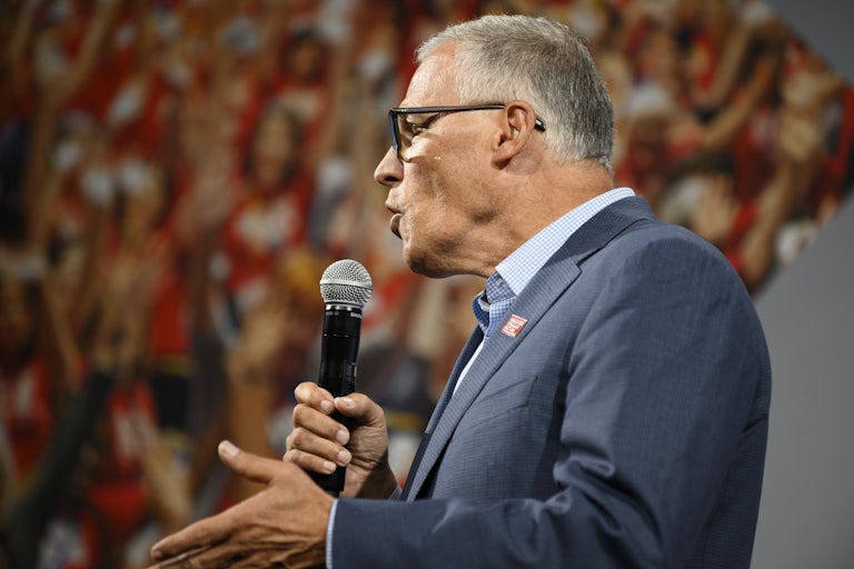 Jay Inslee holds a microphone and speaks at an event.