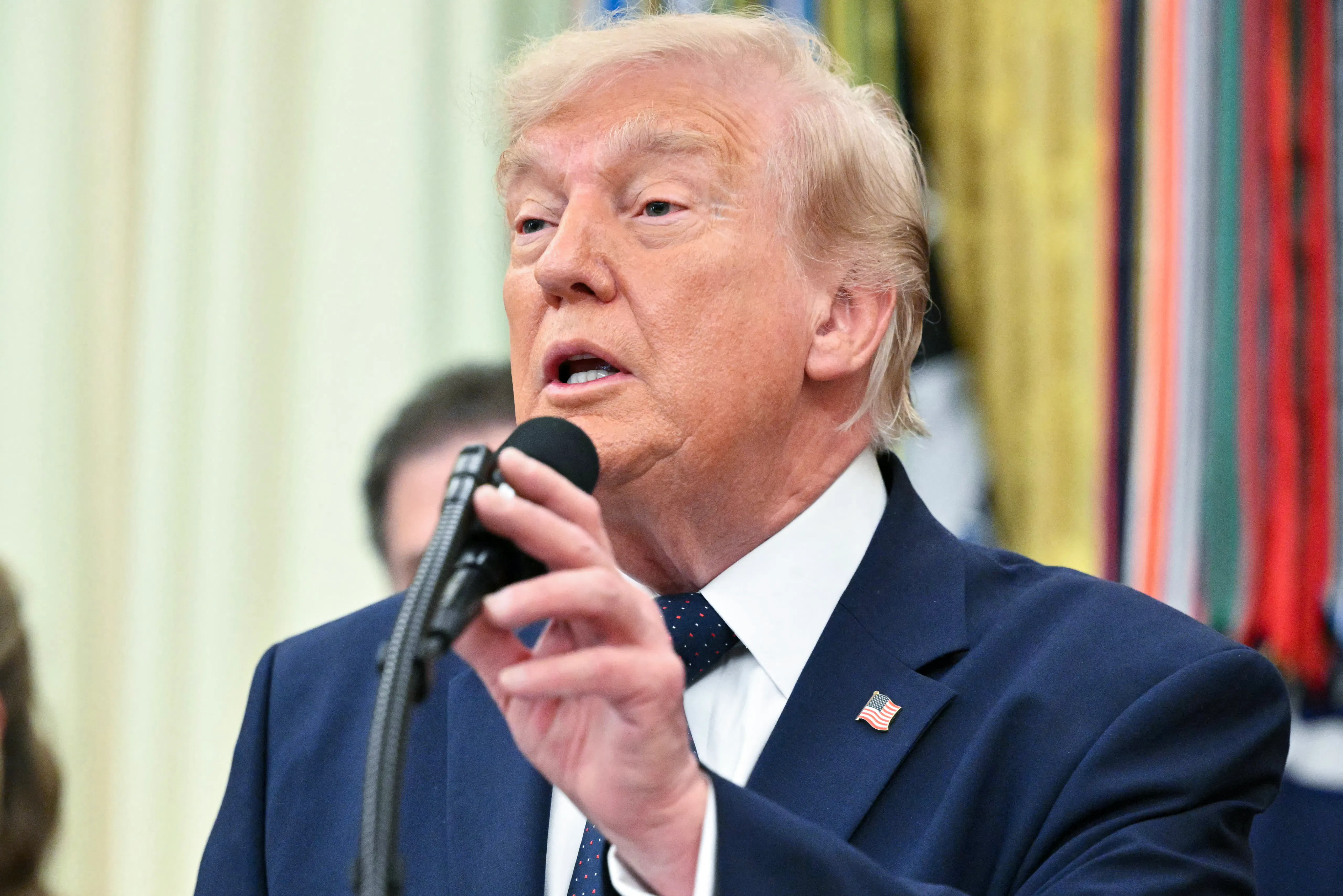 Donald Trump touches the microphone on a podium while speaking during an event in the Oval Office