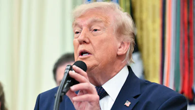 Donald Trump touches the microphone on a podium while speaking during an event in the Oval Office