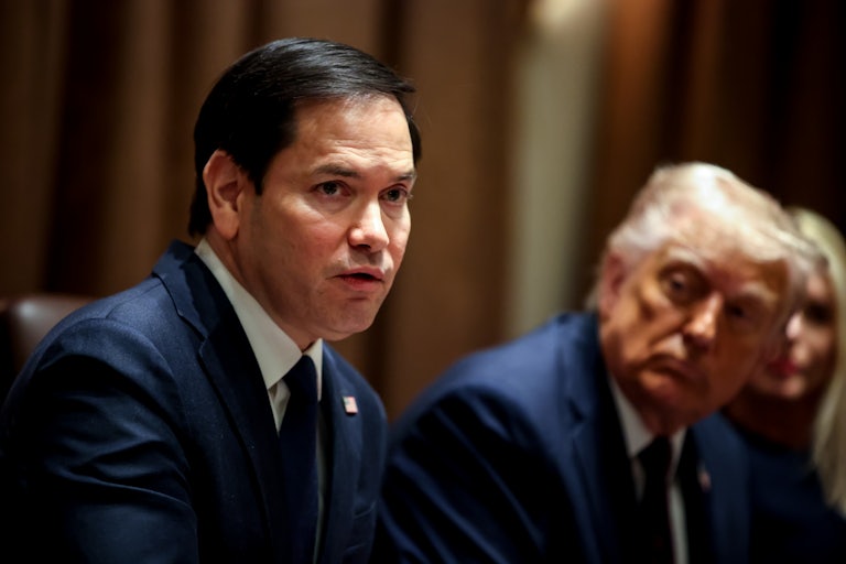 Secretary of State Marco Rubio speaks at a Cabinet meeting. Donald Trump can be seen in the background, seated beside him listening.