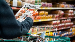 A shopper holds the weekly sales advertisement while pushing their cart in the grocery store.