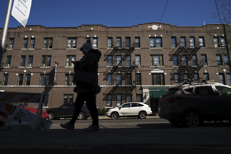 A person in a winter coat and hat walks by a large apartment building in New York City 