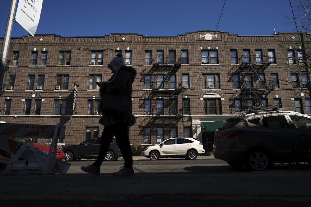 A person in a winter coat and hat walks by a large apartment building in New York City