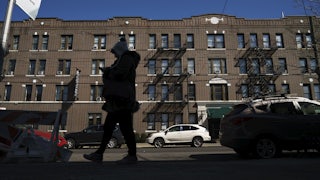 A person in a winter coat and hat walks by a large apartment building in New York City