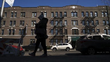 A person in a winter coat and hat walks by a large apartment building in New York City