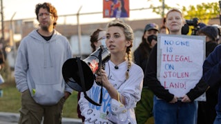 Democratic congressional candidate Kat Abughazaleh holds a megaphone outside of the Broadview ICE processing facility with other protestors visible behind her.