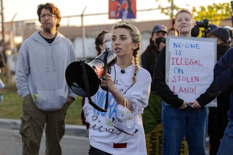 Democratic congressional candidate Kat Abughazaleh holds a megaphone outside of the Broadview ICE processing facility with other protestors visible behind her.