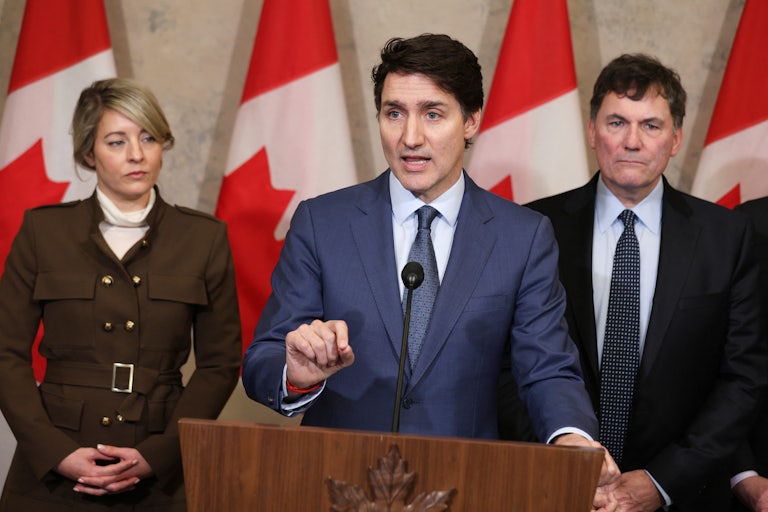 Canadian Prime Minister Justin Trudeau gives a press conference at a podium and points a finger for emphasis. He is flanked by Foreign Minister Melanie Joly and Minister of Finance and Intergovernmental Affairs Dominic Leblanc.