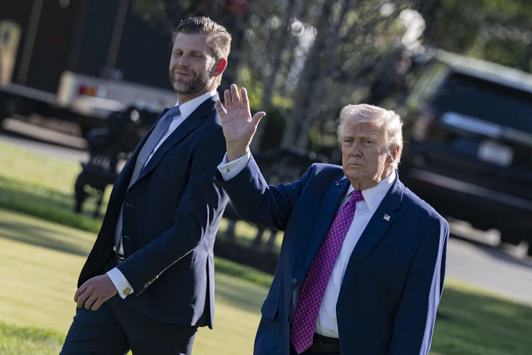 Donald Trump waves while walking next to his son Eric Trump outside the White House