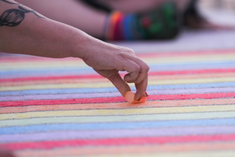 Someone with a flower tattoo on their arm draws a rainbow in chalk.